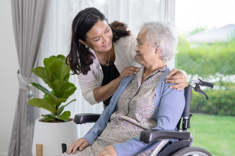 Intrinsic motivation to serve and every action, no matter how small, has the potential to positively impact lives. Smiling middle-aged lady puts her hand on the shoulder of old gray-haired woman in wheelchair to reassure her.